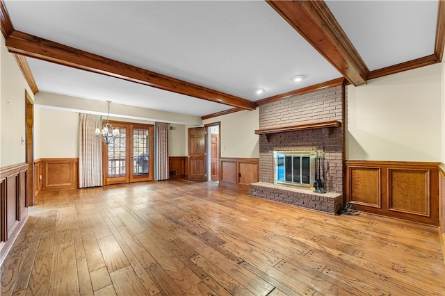 unfurnished living room with a brick fireplace, crown molding, a notable chandelier, beamed ceiling, and light hardwood / wood-style floors