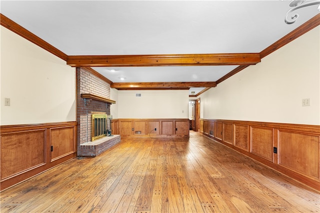 unfurnished living room with a fireplace, beamed ceiling, ornamental molding, and light hardwood / wood-style flooring