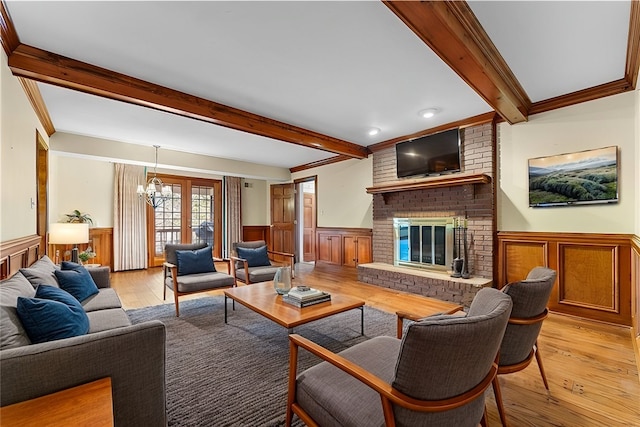 living room featuring a brick fireplace, light hardwood / wood-style flooring, beamed ceiling, a chandelier, and ornamental molding