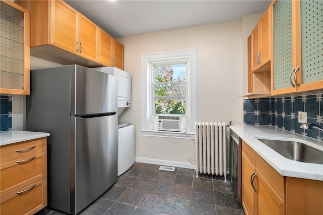 kitchen with sink, radiator heating unit, tasteful backsplash, light stone counters, and appliances with stainless steel finishes