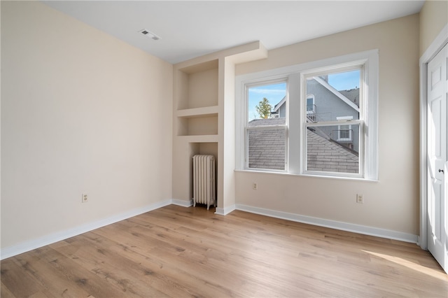 interior space featuring built in shelves, radiator heating unit, and light hardwood / wood-style flooring