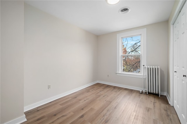 unfurnished bedroom with radiator heating unit, light wood-type flooring, and a closet