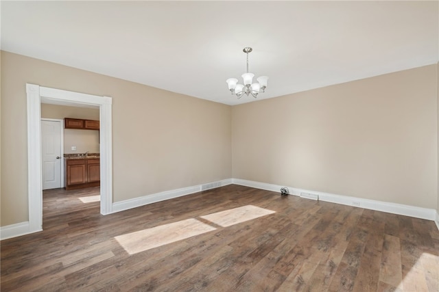 spare room featuring dark wood-type flooring and a notable chandelier