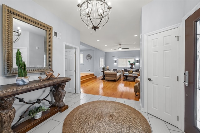 foyer entrance with light hardwood / wood-style flooring and ceiling fan with notable chandelier