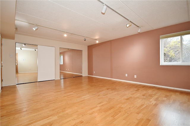 spare room with a textured ceiling, light hardwood / wood-style floors, and rail lighting