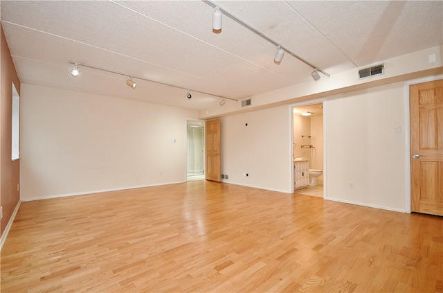 spare room with a textured ceiling, light wood-type flooring, and rail lighting