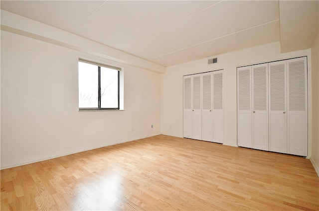 unfurnished bedroom featuring light wood-type flooring and multiple closets