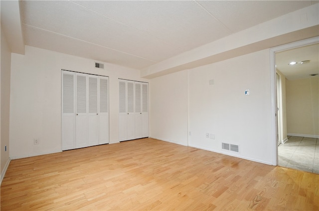 unfurnished bedroom with two closets and light hardwood / wood-style flooring