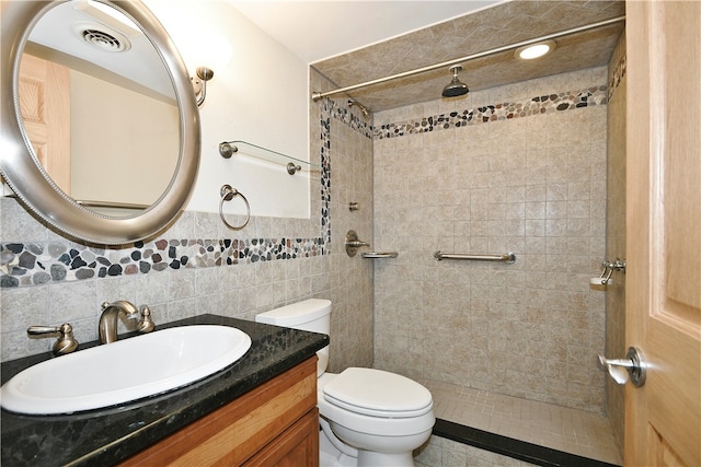 bathroom with vanity, toilet, a tile shower, and tile walls