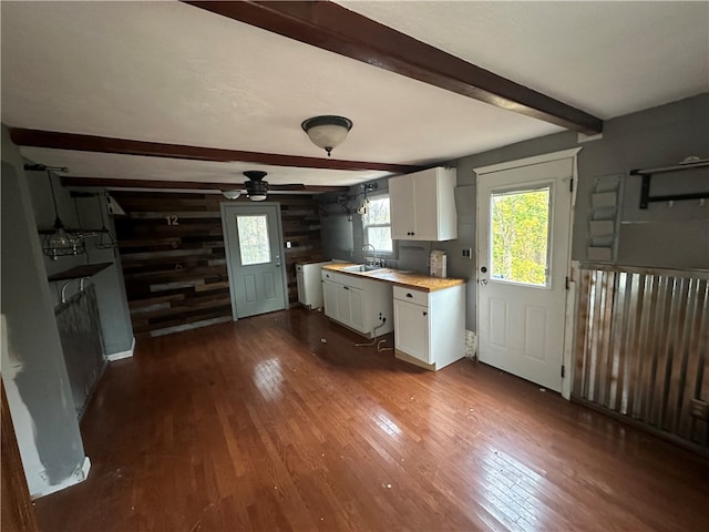 kitchen with wood walls, dark wood-type flooring, white cabinets, sink, and butcher block countertops