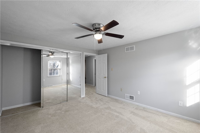 unfurnished bedroom with a textured ceiling, ceiling fan, a closet, and light colored carpet