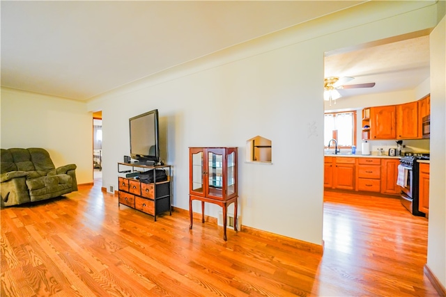 living room with light wood-type flooring, ceiling fan, and sink