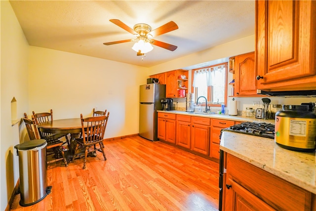 kitchen with sink, light hardwood / wood-style flooring, ceiling fan, light stone countertops, and stainless steel refrigerator