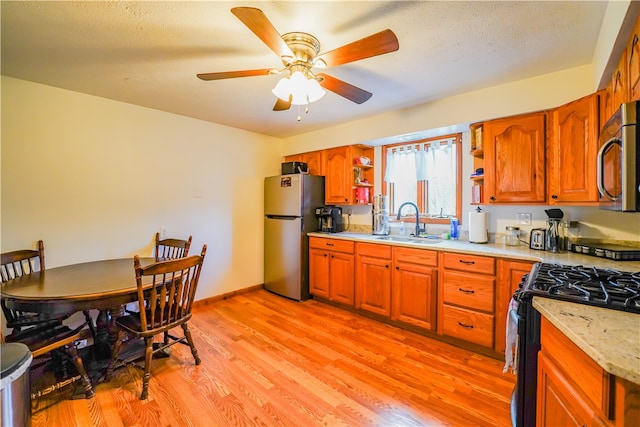 kitchen with ceiling fan, sink, light hardwood / wood-style flooring, a textured ceiling, and appliances with stainless steel finishes