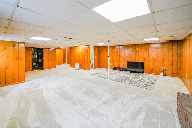 basement with a paneled ceiling, wooden walls, and carpet