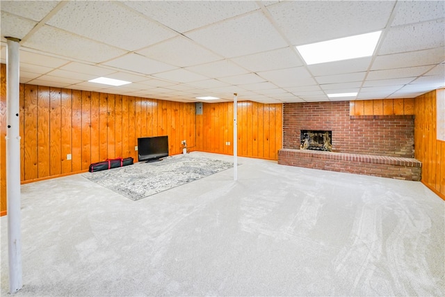 basement with a paneled ceiling, wooden walls, a fireplace, and carpet floors