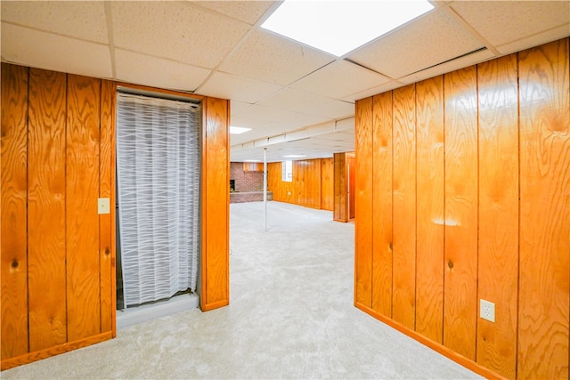 hall with light colored carpet, a drop ceiling, and wooden walls