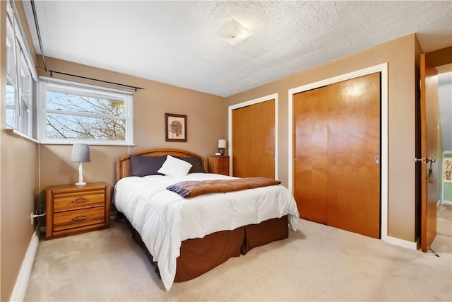 bedroom with a textured ceiling, light colored carpet, and multiple closets