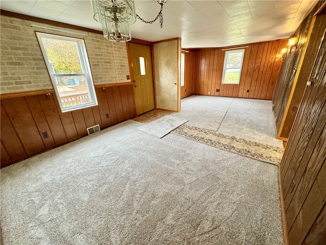 foyer featuring a chandelier, light colored carpet, brick wall, and wood walls