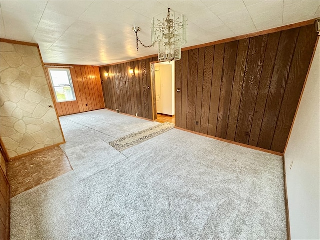 unfurnished room featuring a chandelier, light colored carpet, and wooden walls