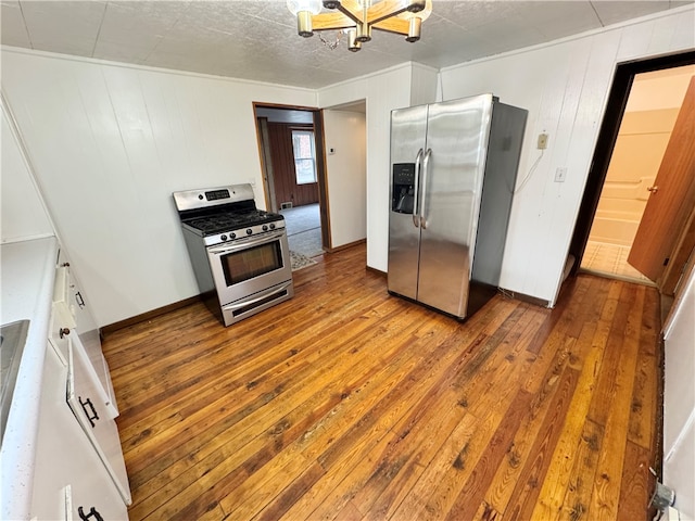 kitchen with hardwood / wood-style floors, a chandelier, wooden walls, white cabinets, and appliances with stainless steel finishes