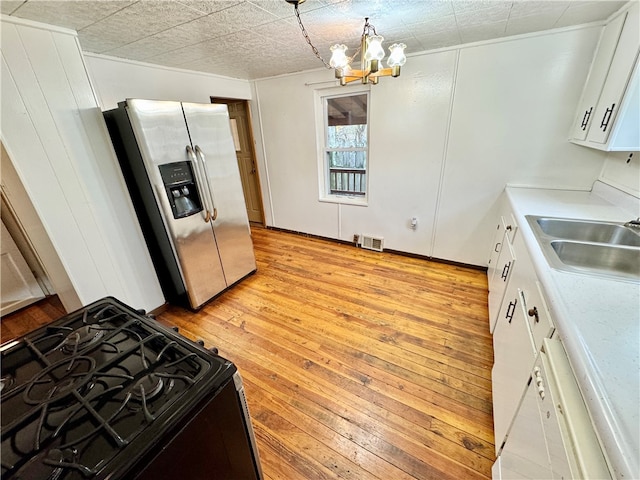 kitchen featuring white cabinets, sink, stainless steel fridge, light wood-type flooring, and black range with gas cooktop