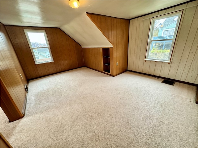 bonus room featuring light carpet, vaulted ceiling, and wood walls