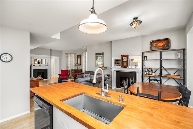 kitchen with wooden counters, sink, decorative light fixtures, light hardwood / wood-style flooring, and dishwasher