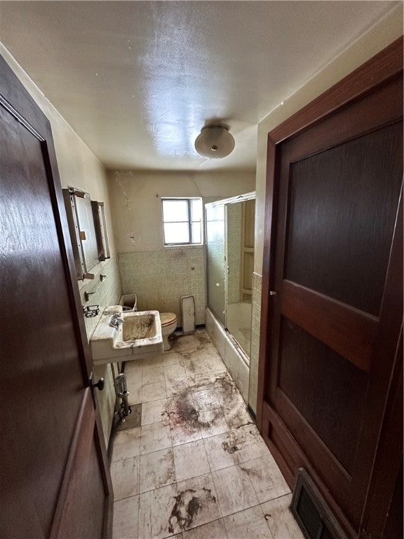 bathroom featuring toilet and bath / shower combo with glass door