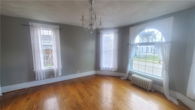 unfurnished dining area with a chandelier, radiator heating unit, and hardwood / wood-style floors