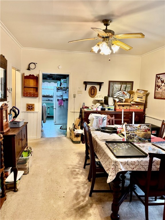 carpeted dining space featuring ceiling fan and crown molding