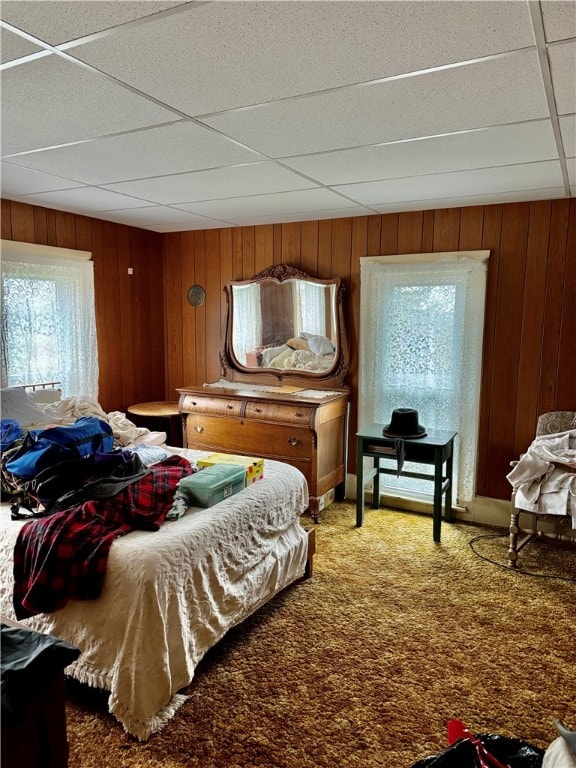 bedroom featuring carpet, a drop ceiling, and wood walls