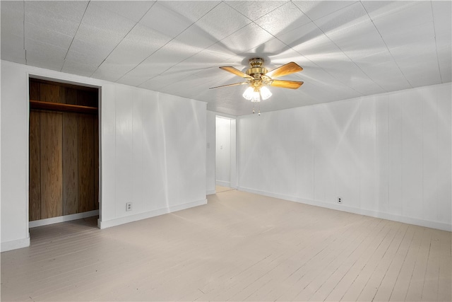 interior space with light wood-type flooring, a closet, ceiling fan, and wood walls