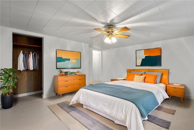 bedroom featuring ceiling fan, light hardwood / wood-style floors, wooden walls, and a closet