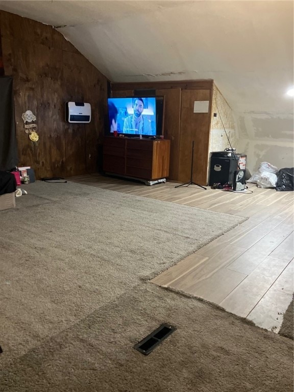 unfurnished living room with light colored carpet, wooden walls, and vaulted ceiling