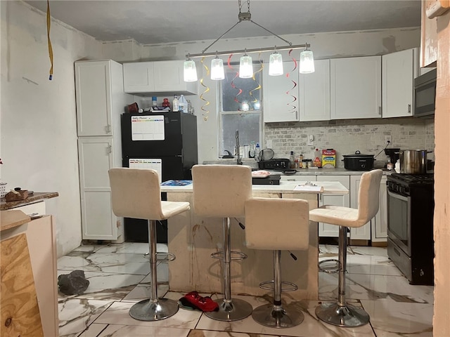 kitchen featuring black appliances, a kitchen breakfast bar, hanging light fixtures, decorative backsplash, and white cabinetry