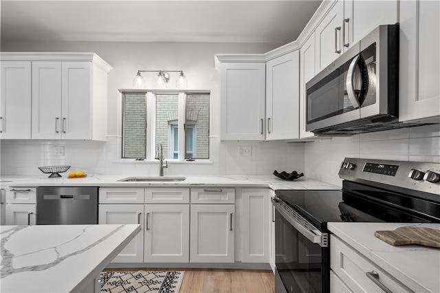 kitchen featuring white cabinetry, sink, stainless steel appliances, backsplash, and light hardwood / wood-style floors