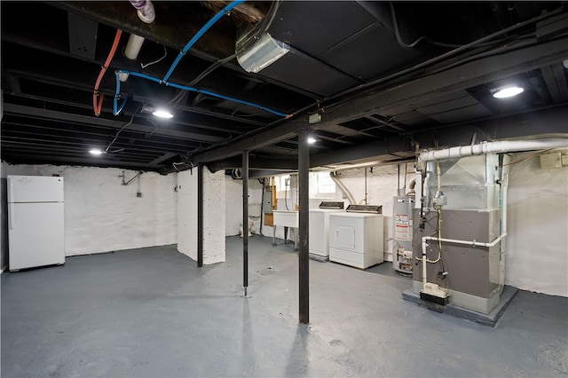 basement featuring heating unit, white refrigerator, independent washer and dryer, and water heater