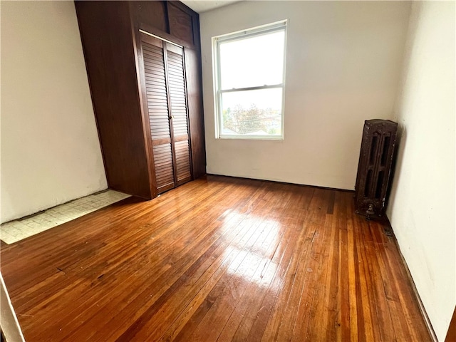 unfurnished bedroom with hardwood / wood-style flooring, radiator heating unit, and a closet