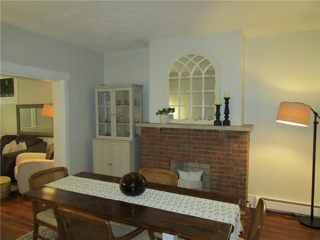 dining room featuring a baseboard heating unit, dark wood-type flooring, and a brick fireplace