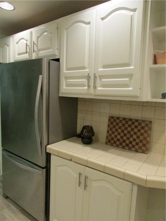 kitchen with white cabinetry, decorative backsplash, tile countertops, and stainless steel refrigerator