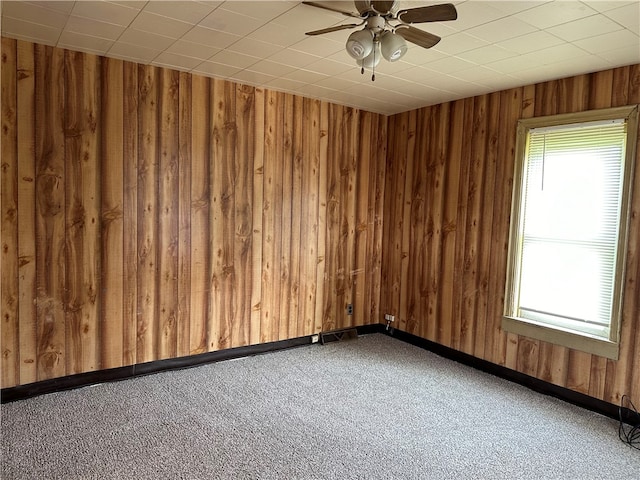 carpeted spare room featuring ceiling fan and wooden walls