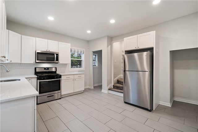 kitchen featuring white cabinets, appliances with stainless steel finishes, light stone counters, and sink