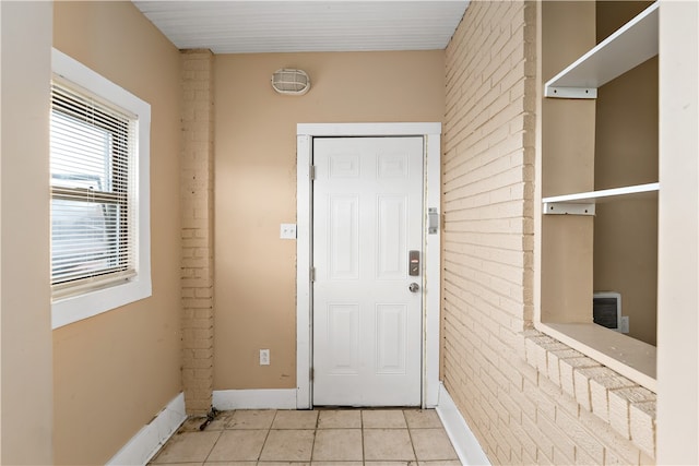 doorway with light tile patterned floors and brick wall