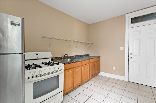 kitchen with stainless steel refrigerator, white gas range, sink, and light tile patterned floors