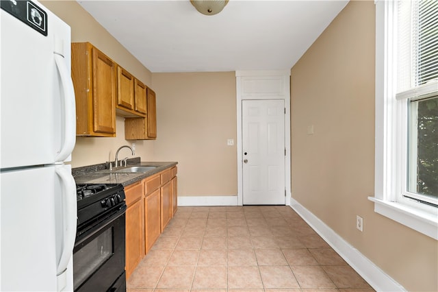 kitchen with black gas range, white fridge, light tile patterned floors, and sink