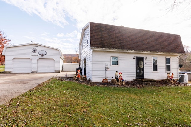 view of front of home with central AC unit, a garage, an outbuilding, and a front lawn