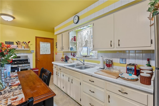 kitchen with white cabinets, gas range, decorative backsplash, and sink