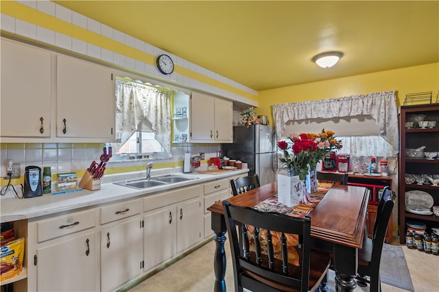 kitchen featuring decorative backsplash, stainless steel fridge, sink, light tile patterned floors, and white cabinets