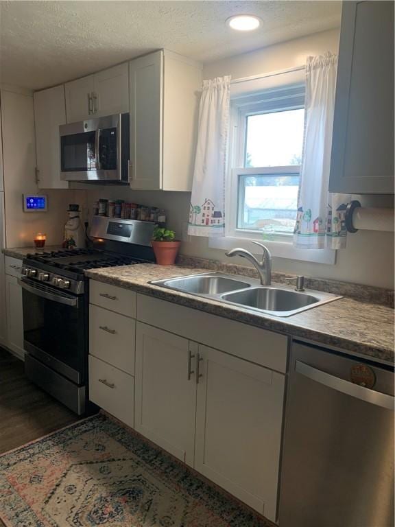 kitchen featuring appliances with stainless steel finishes, sink, white cabinets, and a textured ceiling